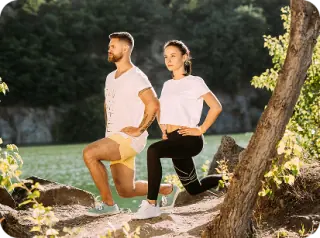 Two people stretching outdoors beside a tree.