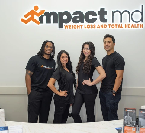 Four Impact MD team members standing beneath the office's Impact MD sign.